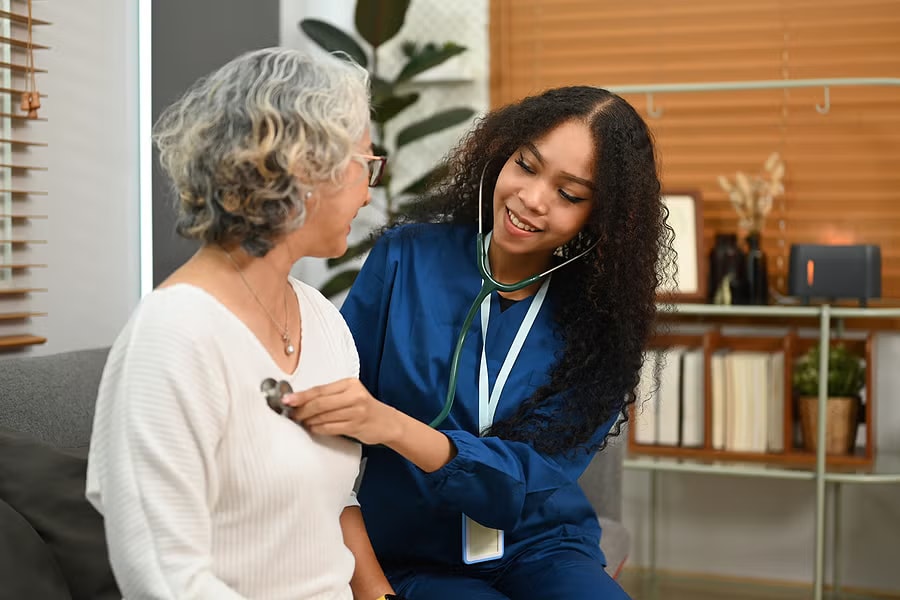 Black nurse examining an older patient at home