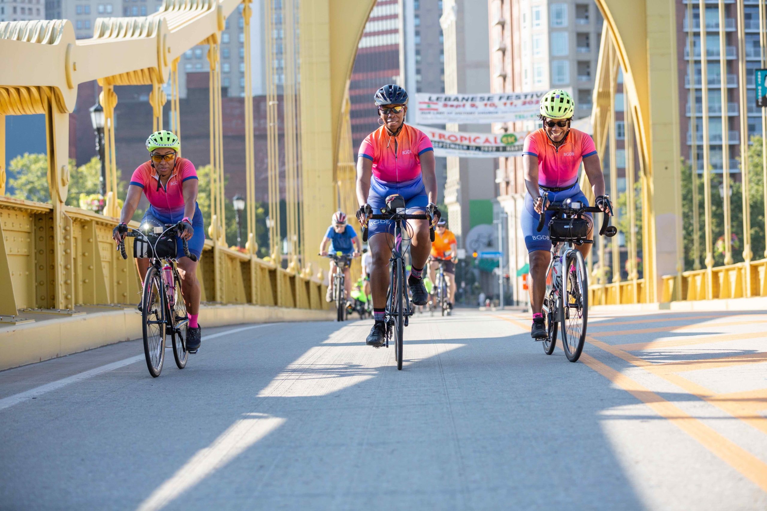 Black Girls Do Bike members riding across a Pittsburgh bridge in matching pink and blue jerseys
