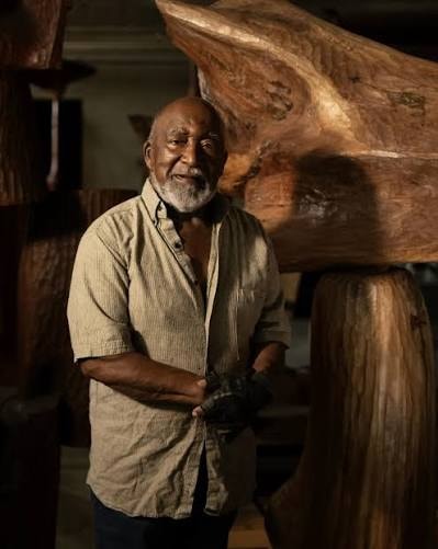 Thaddeus Mosley standing beside one of his large wood sculptures