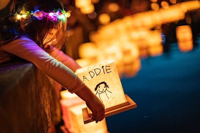 Child with flower crown holding a glowing lantern at Pittsburgh's Night of Light Water Lantern Festival