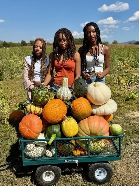 Three women at pumpkin patch with wagon of gourds